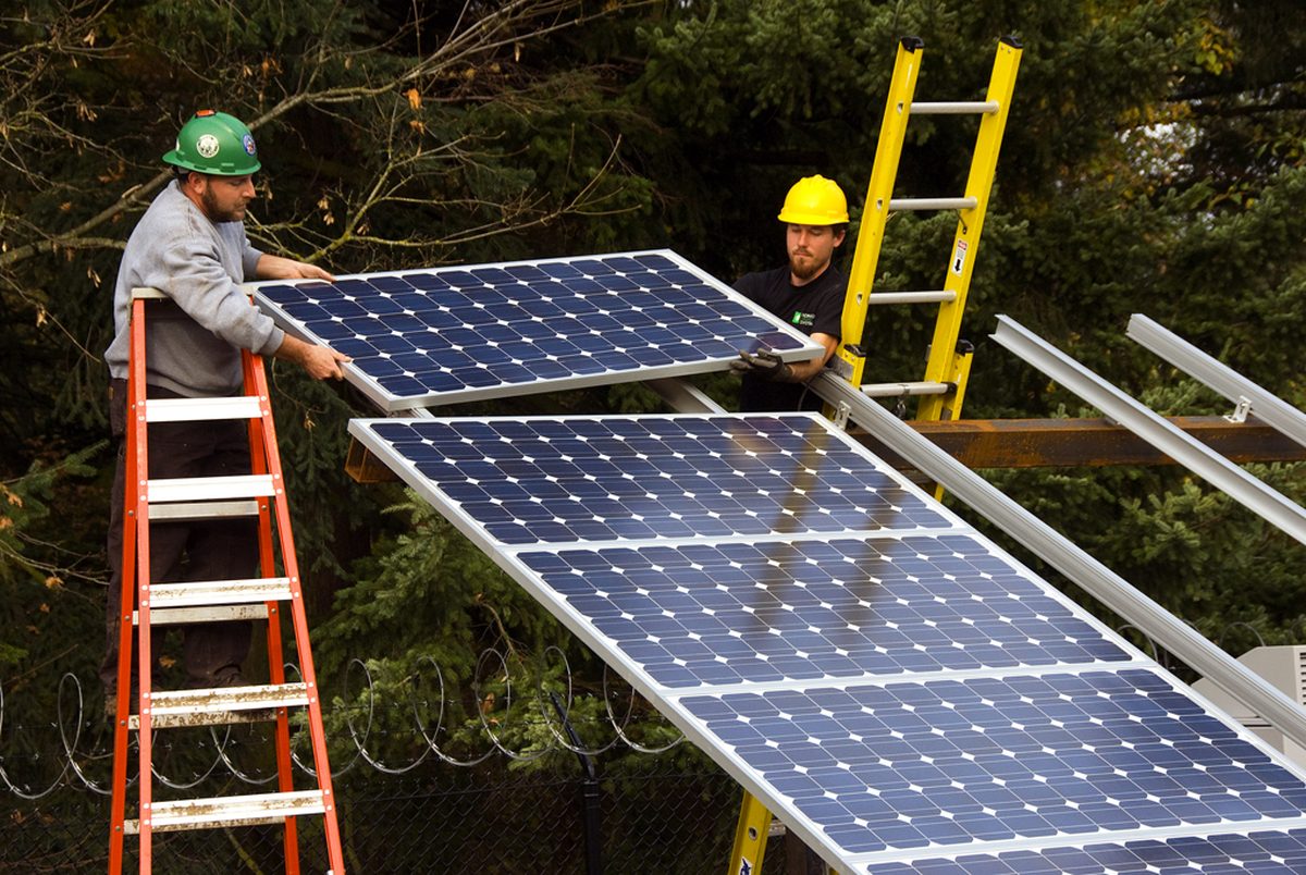 Two workers installing a solar panel on a mounting frame at a solar array construction site