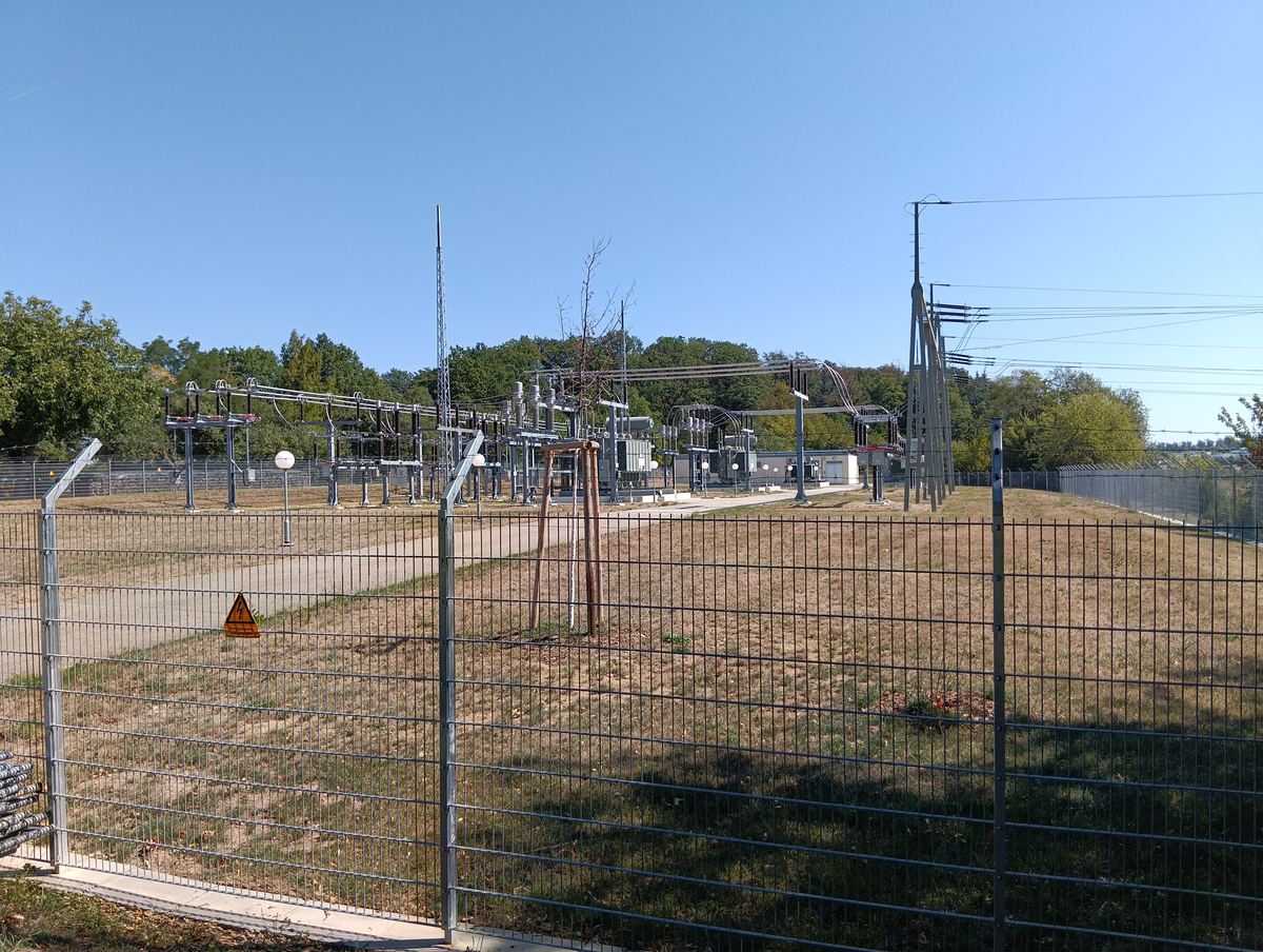 An electrical substation switchyard with busbars, circuit breakers and transmission towers behind a security fence
