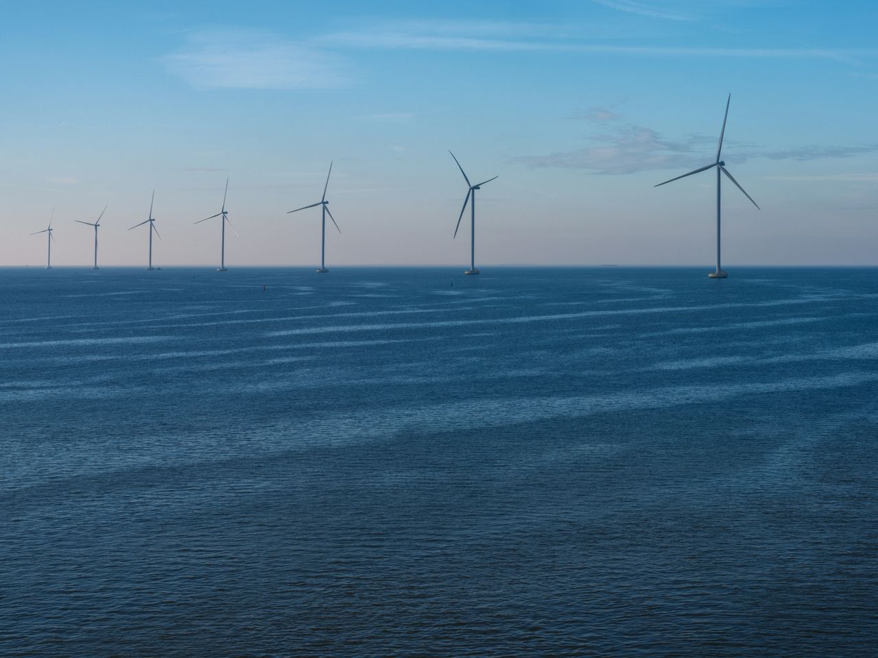 Row of offshore wind turbines standing in the sea at dusk