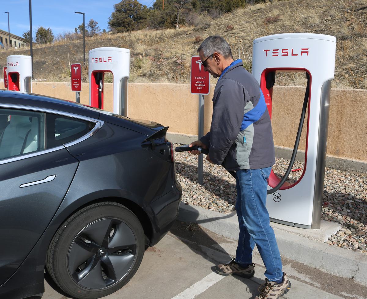 An EV driver connecting a Tesla Supercharger cable to his car.