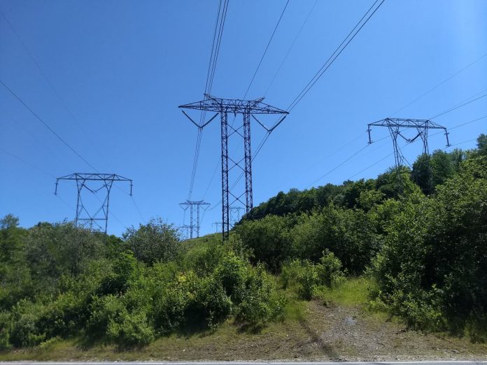 n03-hero A line of high-voltage transmission towers carrying power lines across a forested valley.