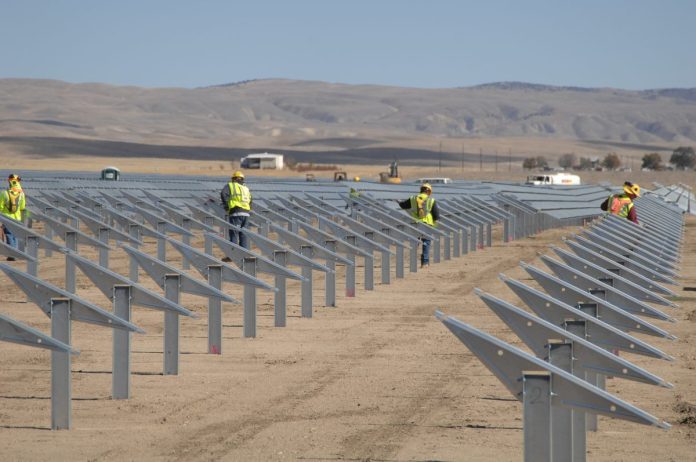 n04-hero Construction workers installing solar-panel racking at a large solar farm in an arid landscape.