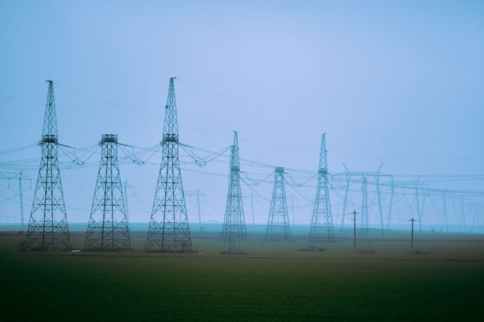 NiSource Microsoft Power Deal: How Indiana Data Centers Could Shave $140 Off Your Annual Electric Bill High-voltage transmission towers crossing a rural field under a blue sky