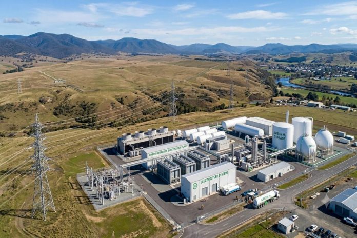 Aerial view of an electrolyser-based green hydrogen production plant with industrial stacks and piping